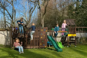 Un espace jeux pour les enfants avec balançoires, mur d'escalade, cabane dans les arbres et trampoline